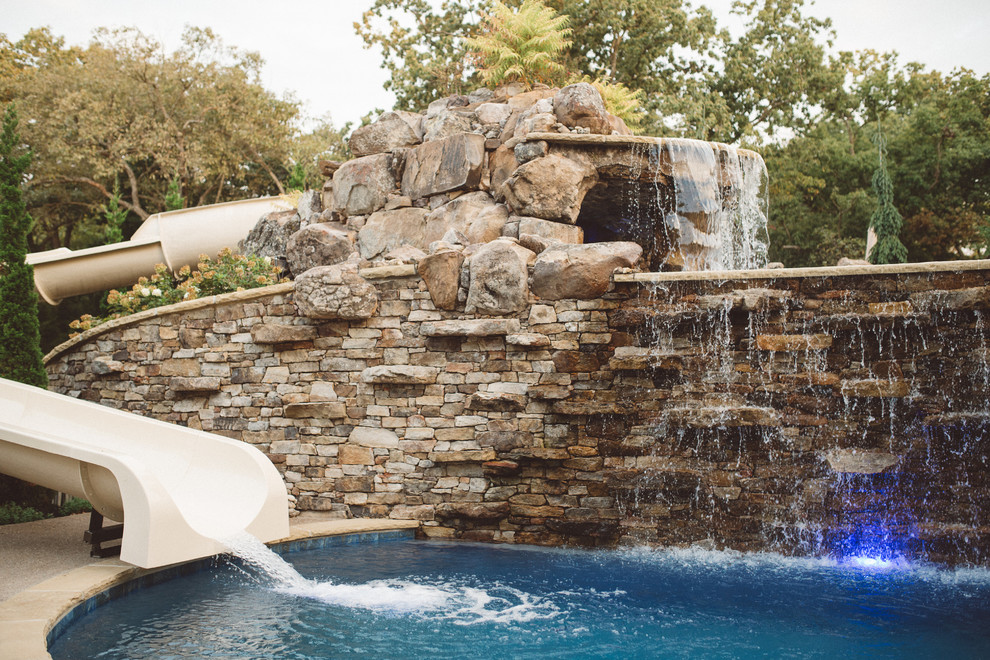 Large traditional back custom shaped swimming pool in Kansas City with a water feature and natural stone paving.