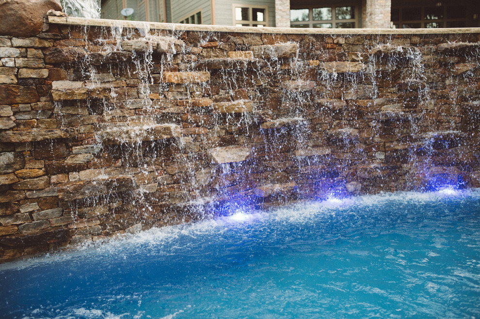 Ejemplo de piscina con fuente de estilo americano grande a medida en patio trasero con adoquines de piedra natural