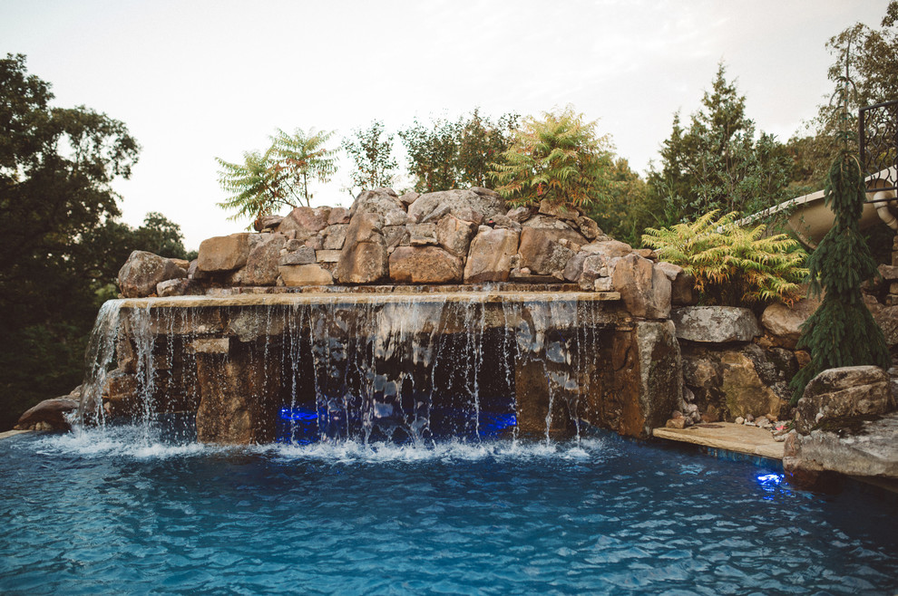 This is an example of a large traditional back custom shaped swimming pool in Kansas City with a water feature.