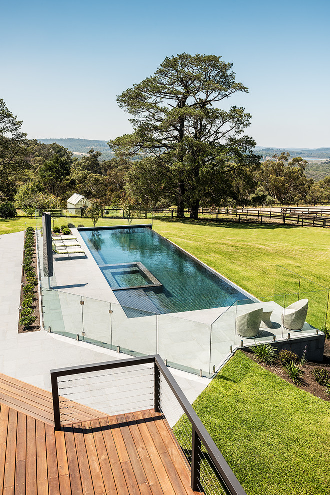 Esempio di un'ampia piscina a sfioro infinito contemporanea rettangolare dietro casa con pavimentazioni in pietra naturale