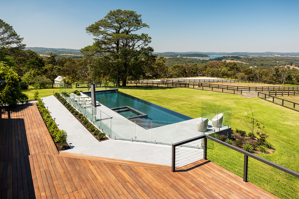 Ejemplo de piscina infinita actual extra grande rectangular en patio trasero con adoquines de piedra natural