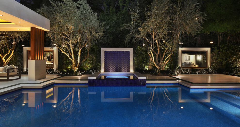 Cette image montre une grande piscine arrière design rectangle avec un point d'eau et des pavés en pierre naturelle.