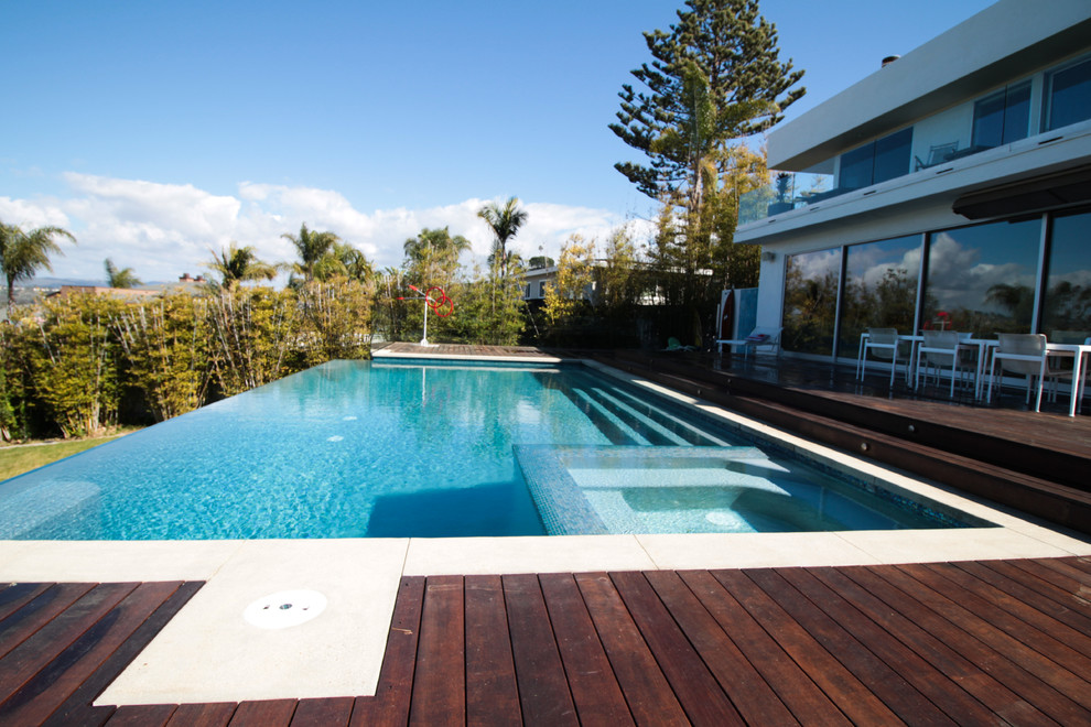 Esempio di una grande piscina a sfioro infinito minimalista rettangolare dietro casa con una vasca idromassaggio e pedane