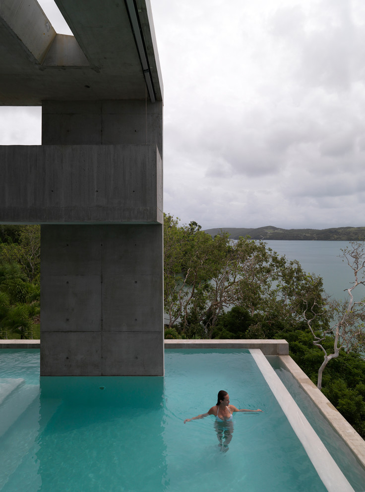 Ispirazione per un'ampia piscina a sfioro infinito industriale a "L" dietro casa con lastre di cemento