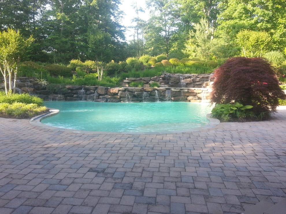 Ejemplo de piscina con fuente alargada tradicional grande a medida en patio trasero con adoquines de piedra natural