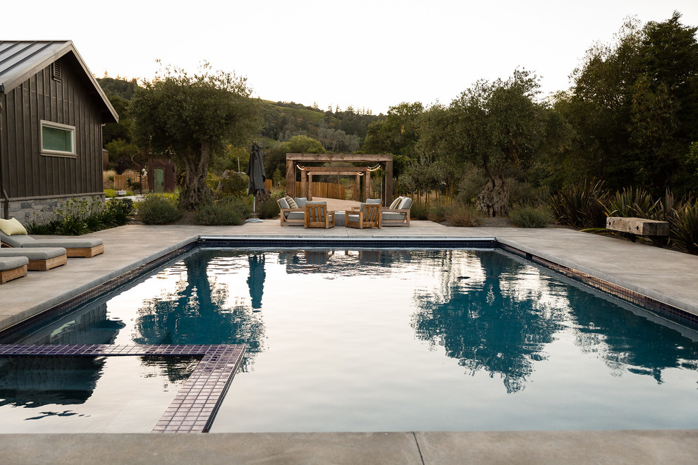 Esempio di una piscina country rettangolare con una vasca idromassaggio e lastre di cemento