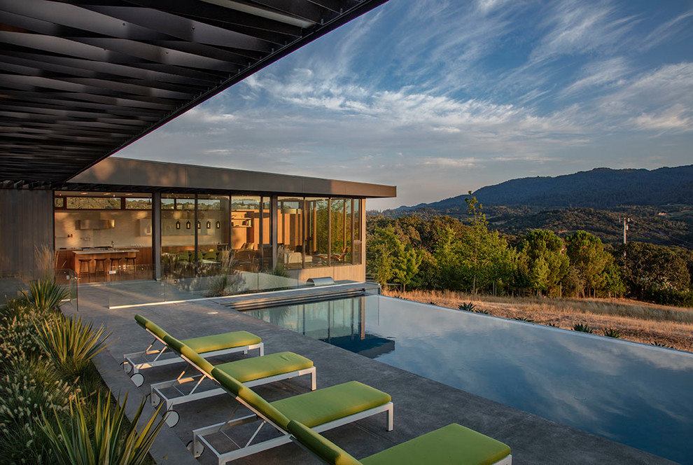 Modelo de piscina infinita contemporánea grande rectangular en patio lateral con losas de hormigón