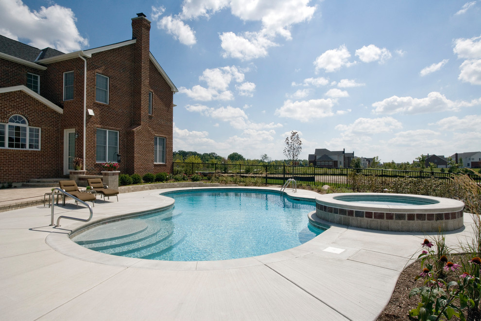 Foto di una piscina naturale classica a "C" di medie dimensioni e dietro casa con una vasca idromassaggio e lastre di cemento