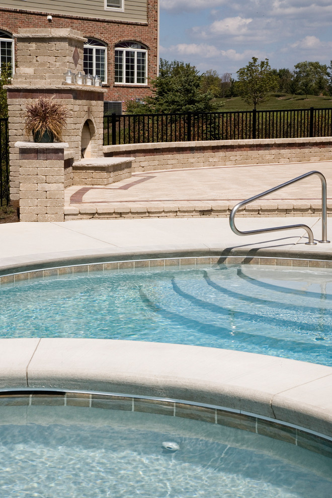 Foto di una piscina naturale chic a "C" di medie dimensioni e dietro casa con una vasca idromassaggio e lastre di cemento