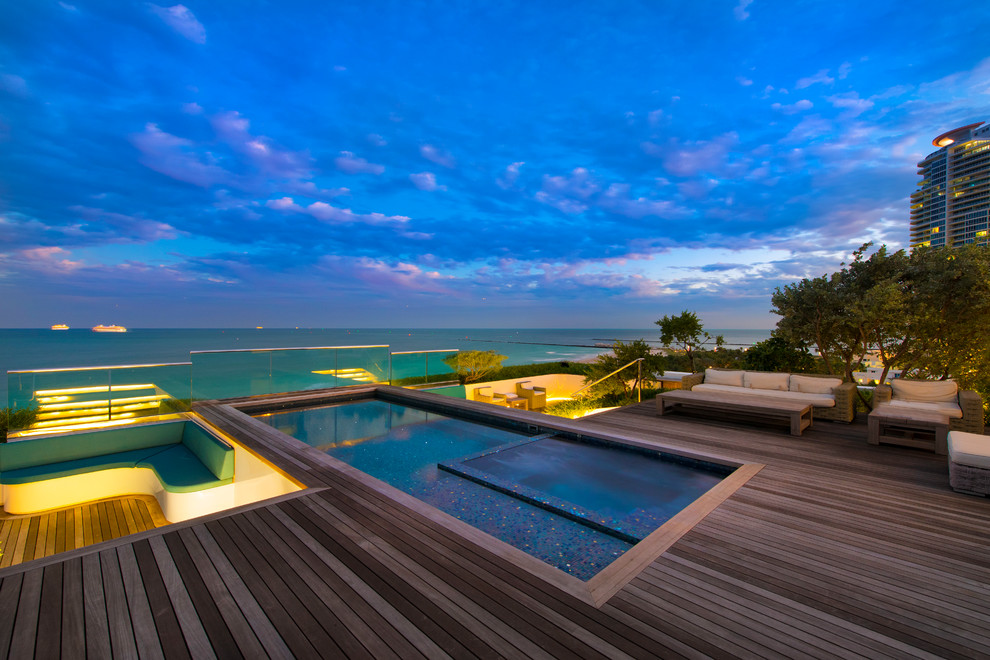 Cette image montre une grande piscine minimaliste rectangle avec un bain bouillonnant et une terrasse en bois.