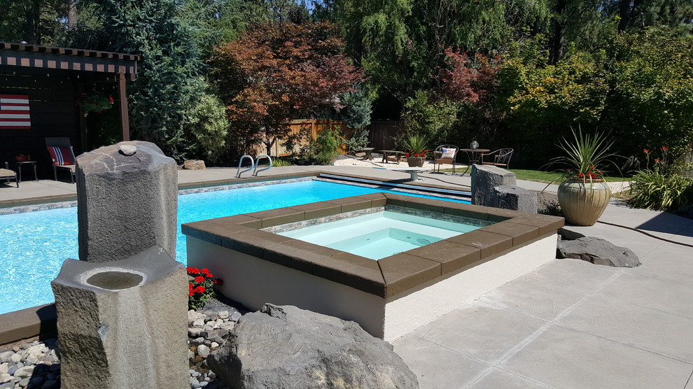 Large modern back rectangular natural swimming pool in Seattle with concrete slabs.