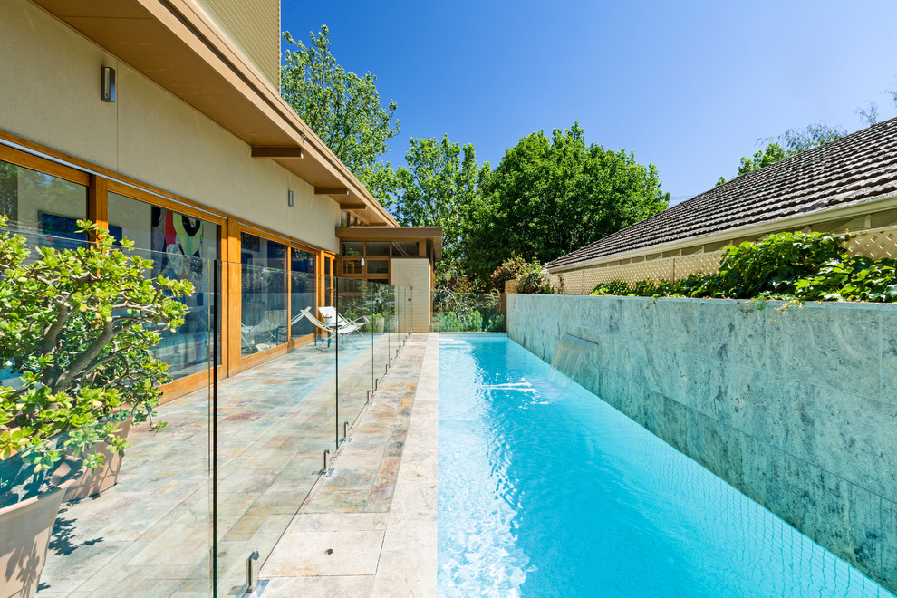 Imagen de piscina alargada moderna rectangular en patio lateral con adoquines de piedra natural