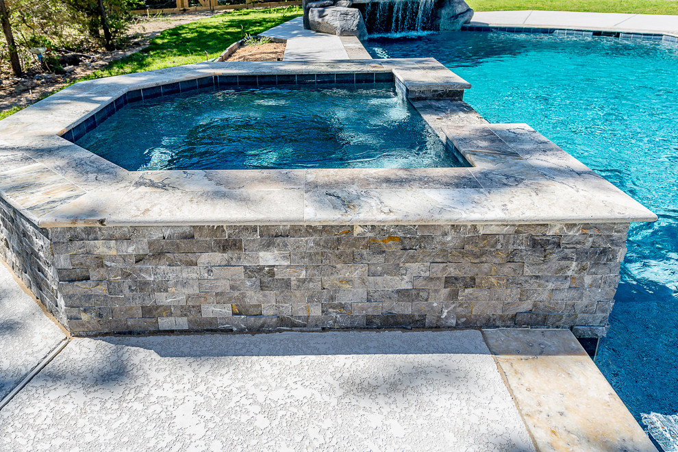 Immagine di una grande piscina naturale chic personalizzata dietro casa con una vasca idromassaggio e lastre di cemento