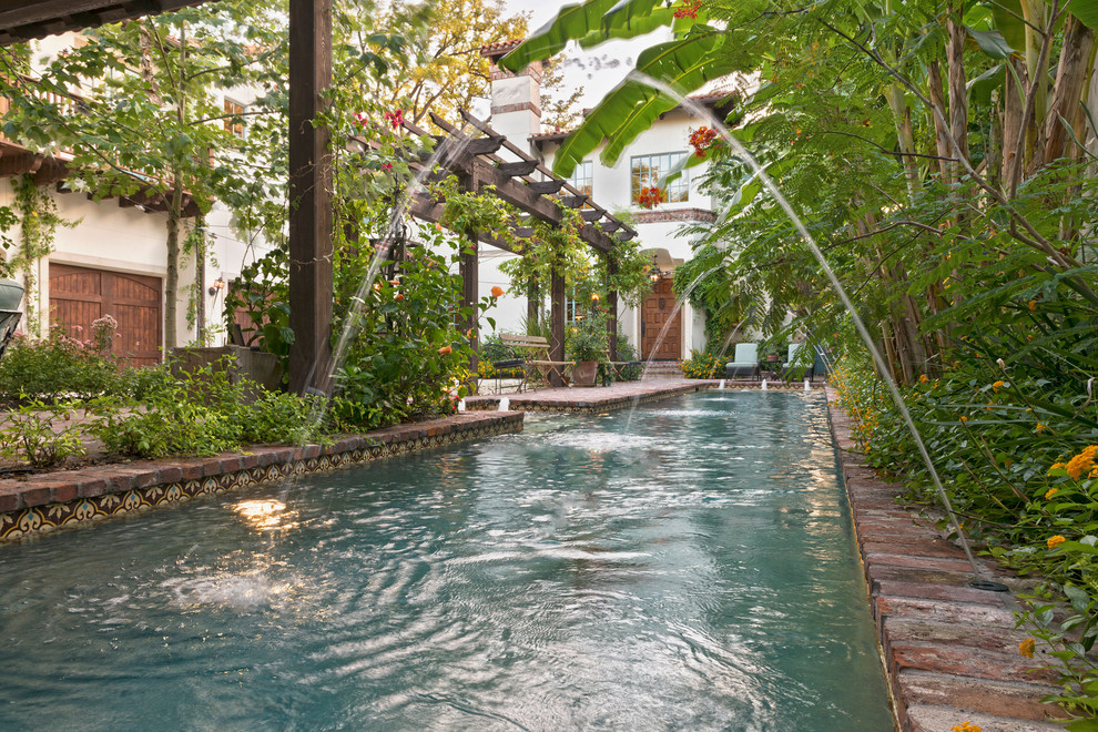 Ejemplo de piscina con fuente alargada mediterránea grande rectangular en patio lateral con adoquines de ladrillo