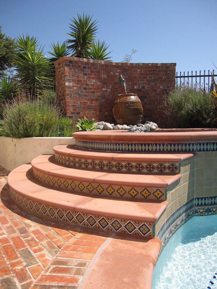 Photo of a mediterranean swimming pool in Orange County with brick paving and a water feature.