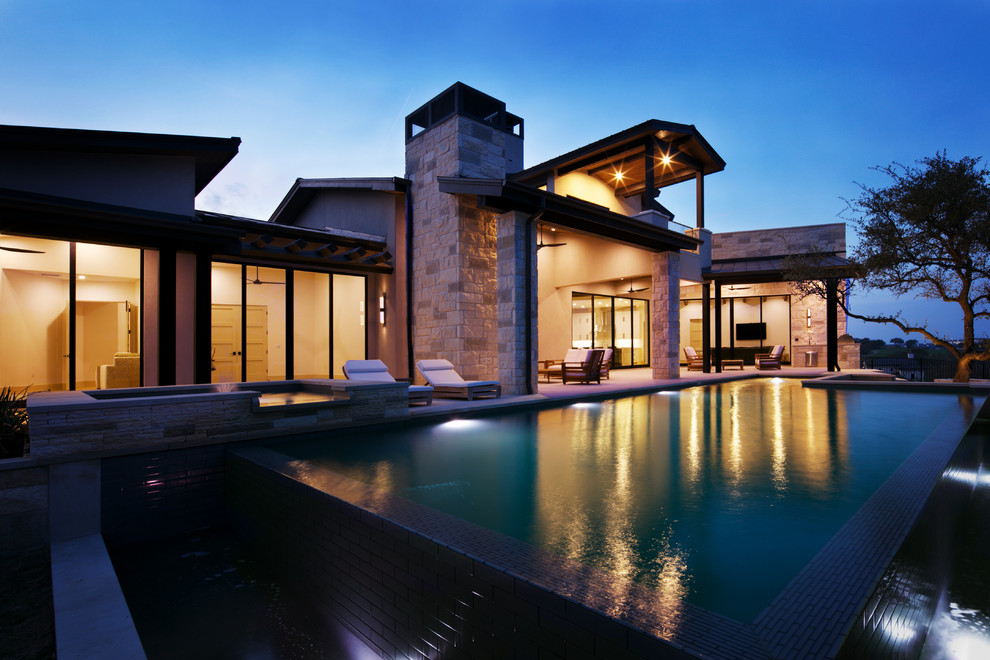 Ispirazione per una grande piscina a sfioro infinito design rettangolare dietro casa con una vasca idromassaggio e pavimentazioni in pietra naturale