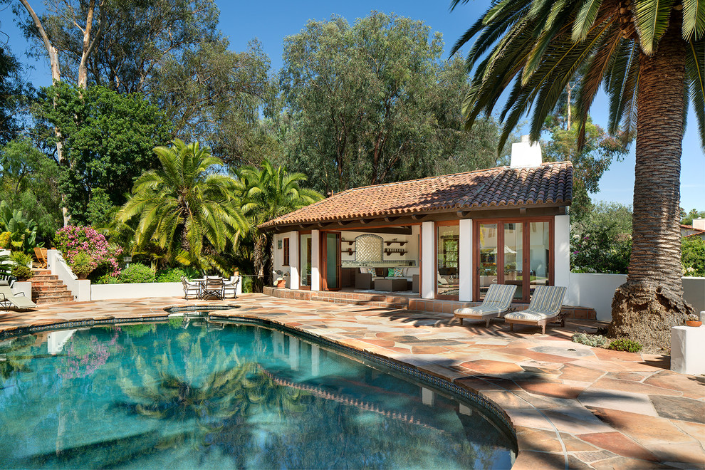 Ejemplo de casa de la piscina y piscina natural de estilo americano redondeada en patio trasero con adoquines de piedra natural