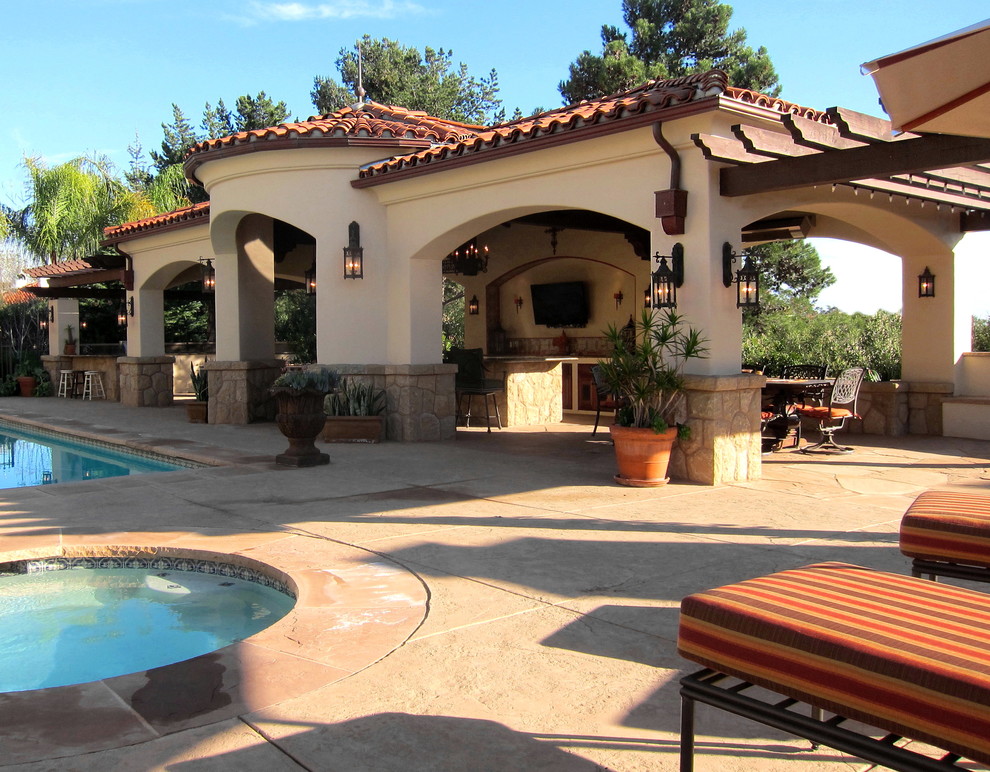 Modelo de casa de la piscina y piscina mediterránea de tamaño medio rectangular en patio trasero con suelo de hormigón estampado