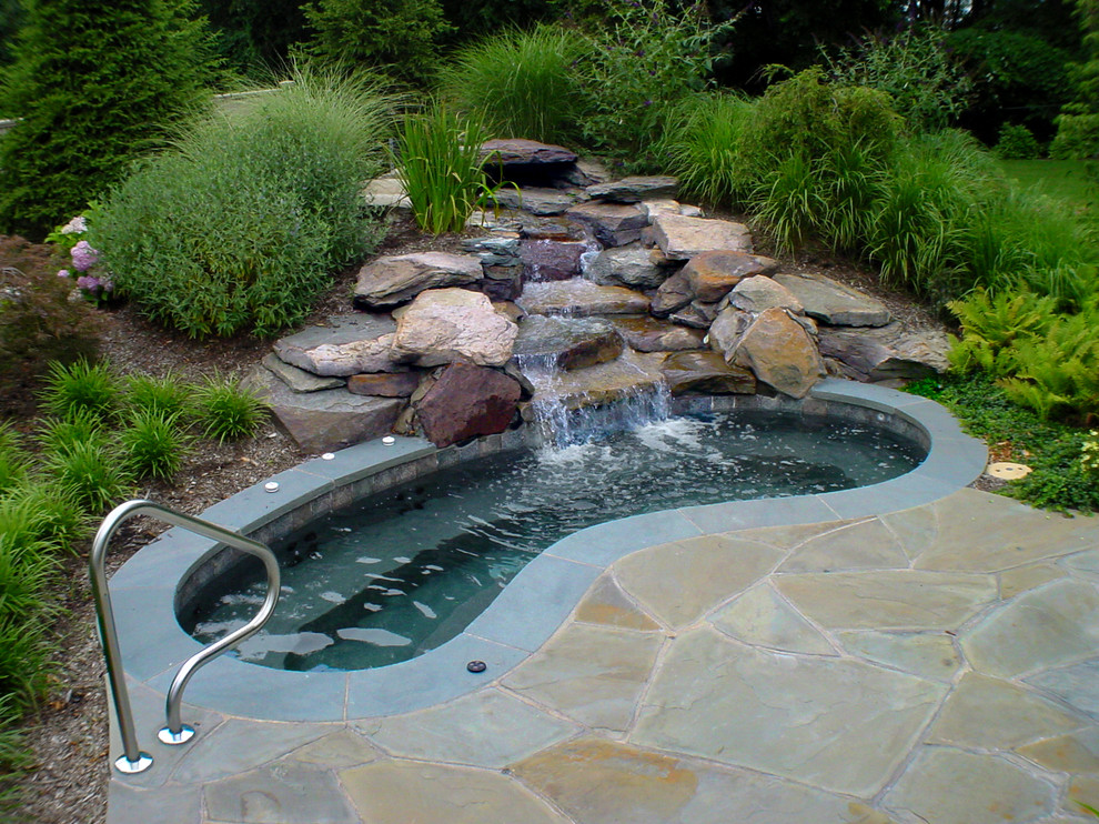 Ejemplo de piscinas y jacuzzis de estilo americano tipo riñón en patio trasero con adoquines de piedra natural