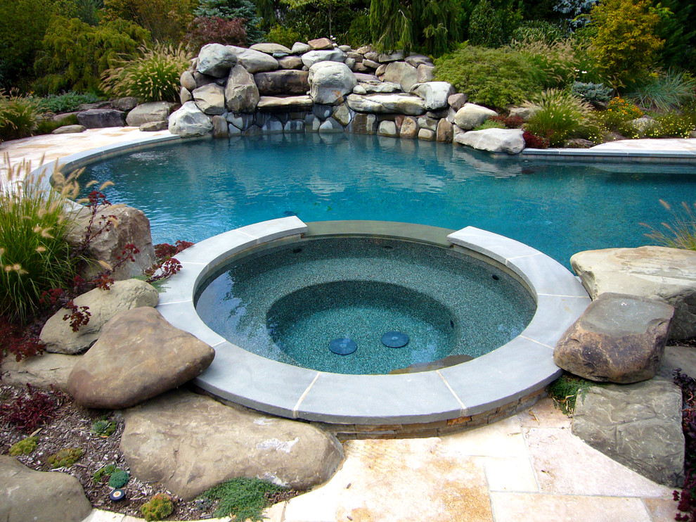 Exempel på en mellanstor amerikansk rund gårdsplan med pool, med spabad och naturstensplattor