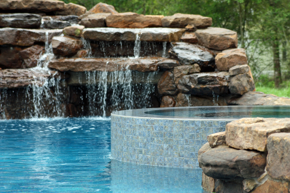 Foto di una grande piscina tradizionale personalizzata dietro casa con pavimentazioni in pietra naturale e una vasca idromassaggio