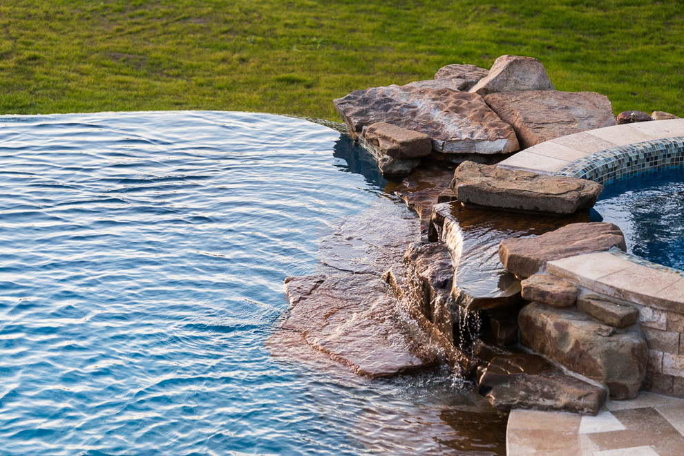 Esempio di un'ampia piscina a sfioro infinito chic personalizzata dietro casa con pavimentazioni in pietra naturale
