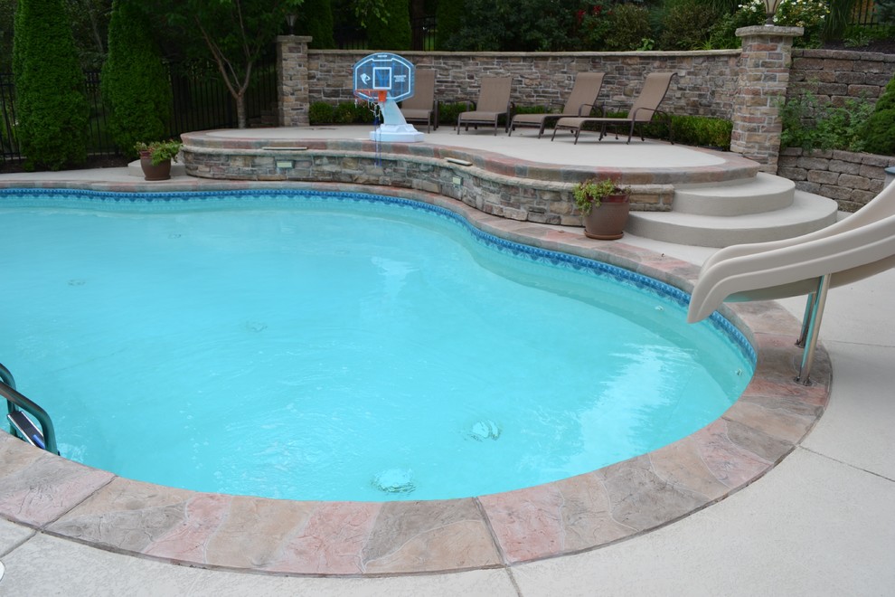 Modelo de piscina natural clásica de tamaño medio a medida en patio trasero con suelo de hormigón estampado