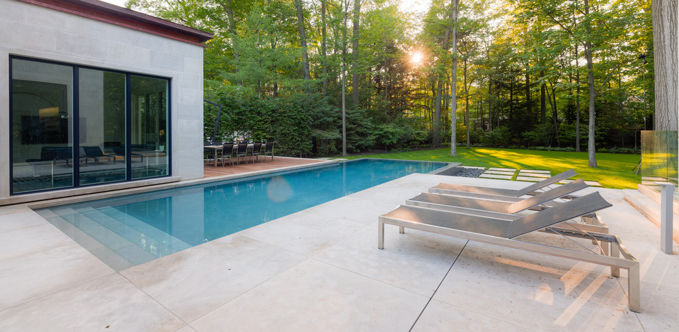 Immagine di una grande piscina a sfioro infinito contemporanea rettangolare dietro casa con fontane e pavimentazioni in pietra naturale