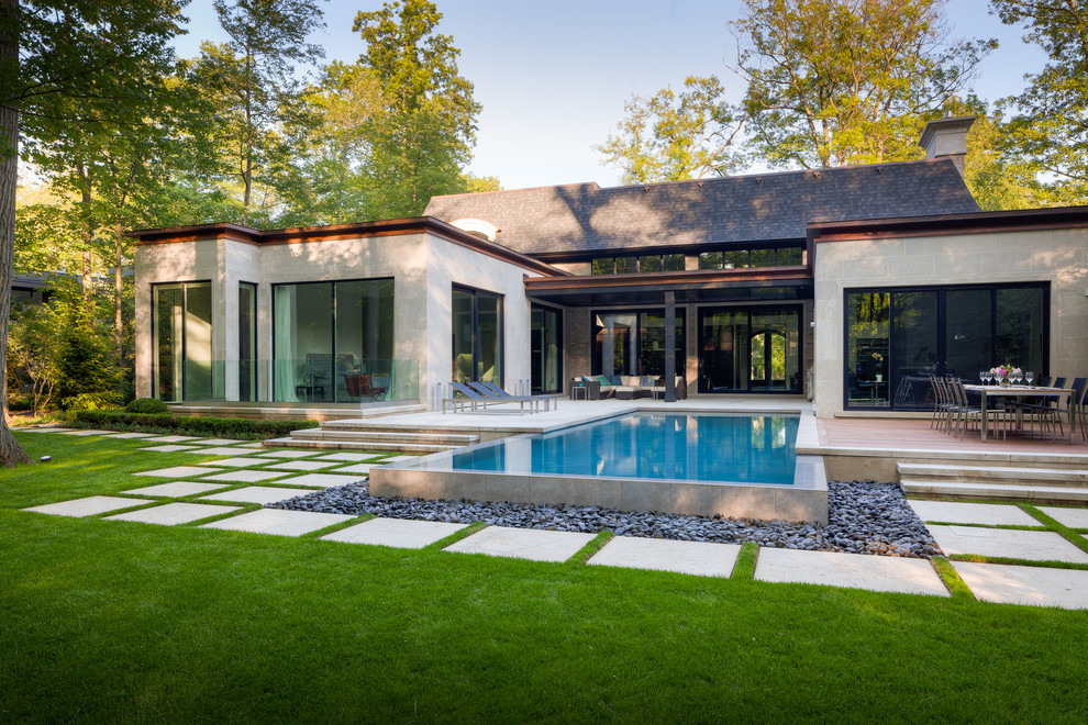 Photo of a large contemporary back rectangular infinity swimming pool in Other with a water feature and natural stone paving.