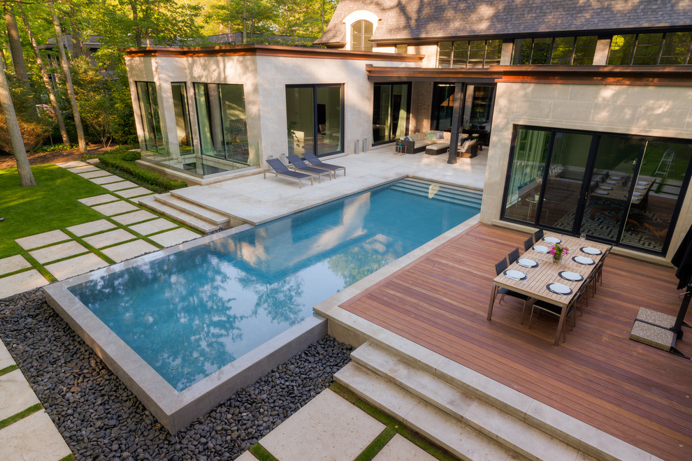 Modelo de piscina con fuente infinita actual grande rectangular en patio trasero con adoquines de piedra natural