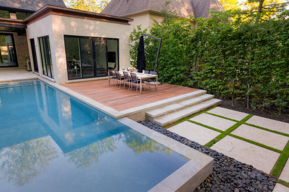 На фото: большой прямоугольный бассейн-инфинити на заднем дворе в современном стиле с фонтаном и покрытием из каменной брусчатки с