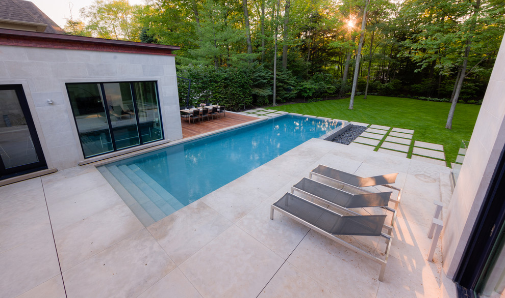 Réalisation d'une grande piscine à débordement et arrière design rectangle avec un point d'eau et des pavés en pierre naturelle.