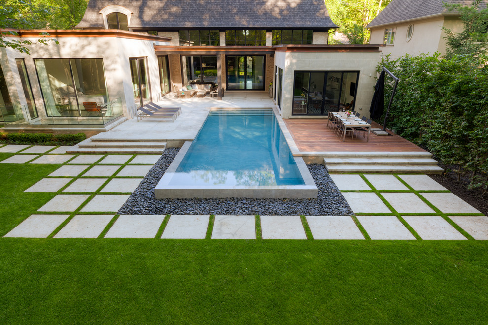 Modelo de piscina con fuente infinita actual grande rectangular en patio trasero con adoquines de piedra natural