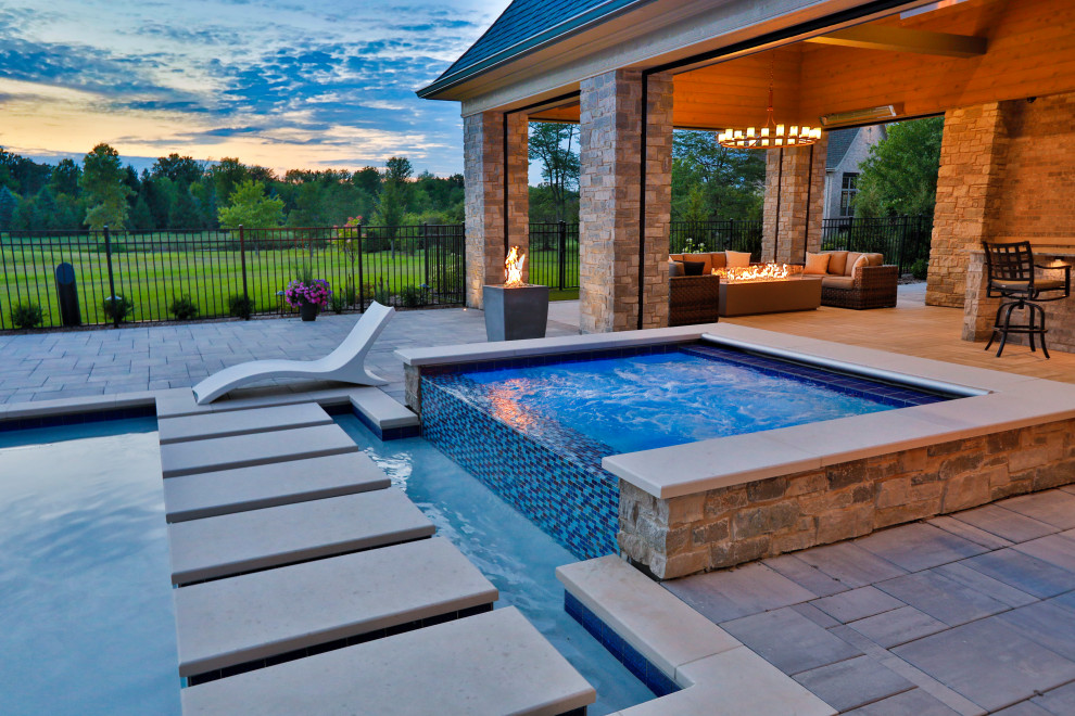Diseño de piscina alargada clásica de tamaño medio rectangular en patio trasero con paisajismo de piscina y adoquines de piedra natural