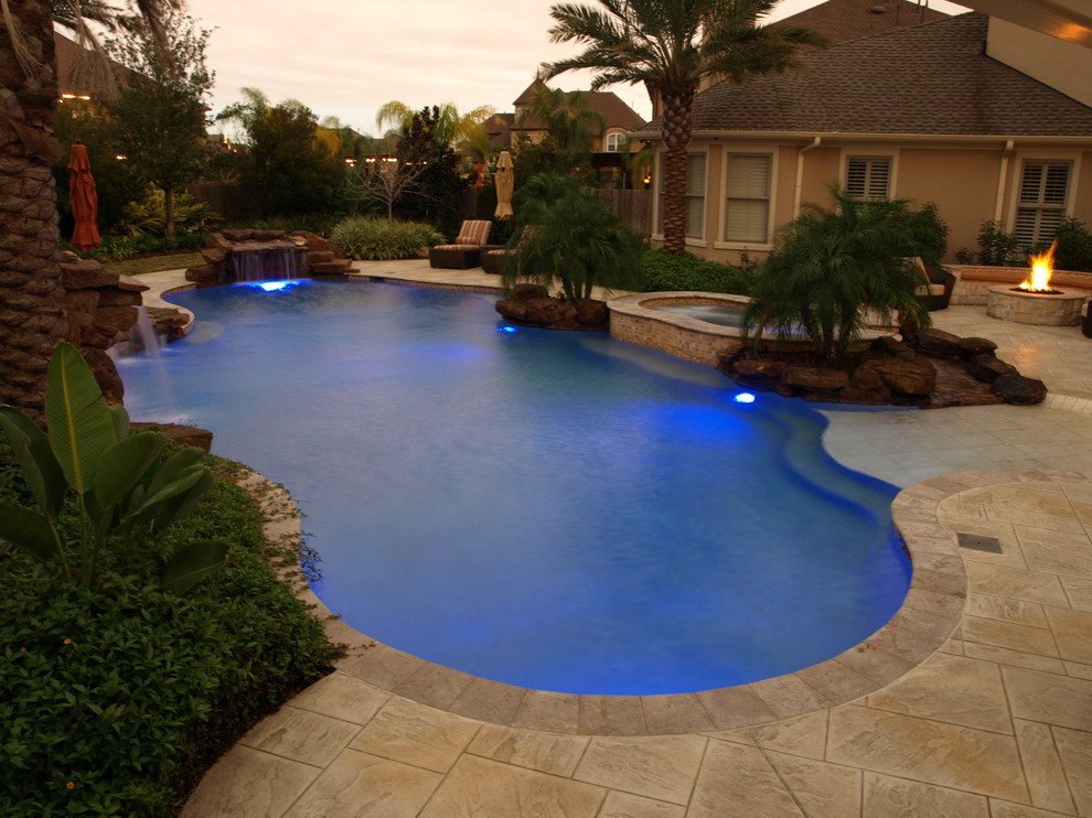 Diseño de piscina con tobogán alargada tropical grande a medida en patio trasero con suelo de baldosas