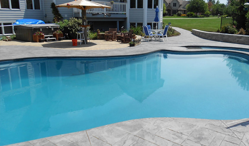 Ejemplo de piscina de estilo americano en patio trasero con adoquines de hormigón