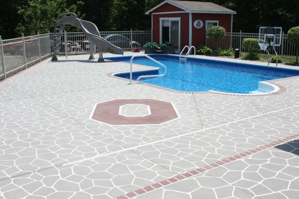 Modelo de piscina con tobogán alargada tradicional de tamaño medio en forma de L en patio trasero con suelo de hormigón estampado