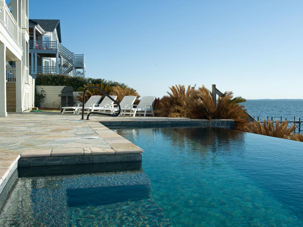 Cette image montre une grande piscine à débordement et arrière design rectangle avec des pavés en pierre naturelle.