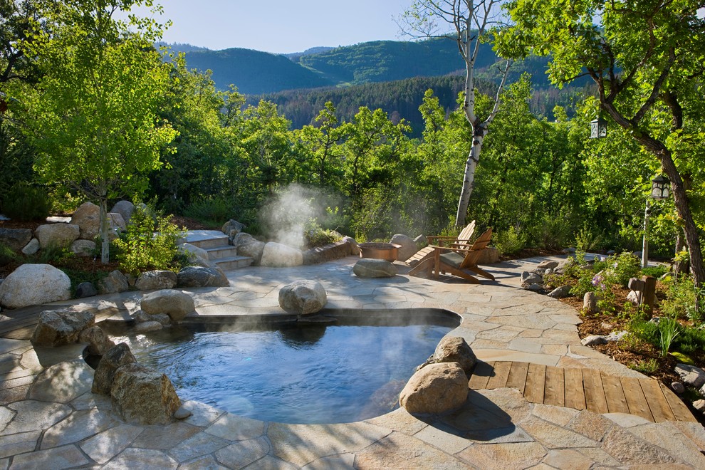 This is an example of a rustic back custom shaped hot tub in Denver with natural stone paving and a shelter.