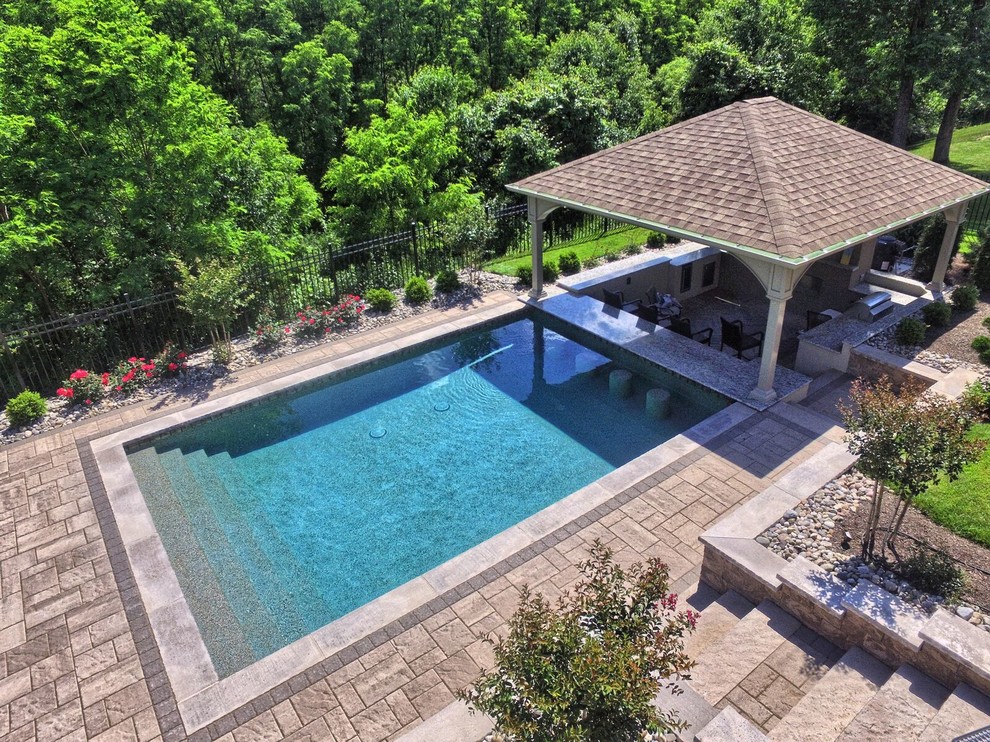 Ejemplo de casa de la piscina y piscina alargada clásica renovada grande rectangular en patio trasero con adoquines de hormigón