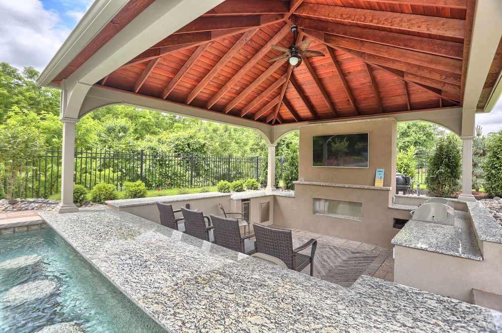 Ejemplo de casa de la piscina y piscina alargada clásica renovada grande rectangular en patio trasero con adoquines de hormigón