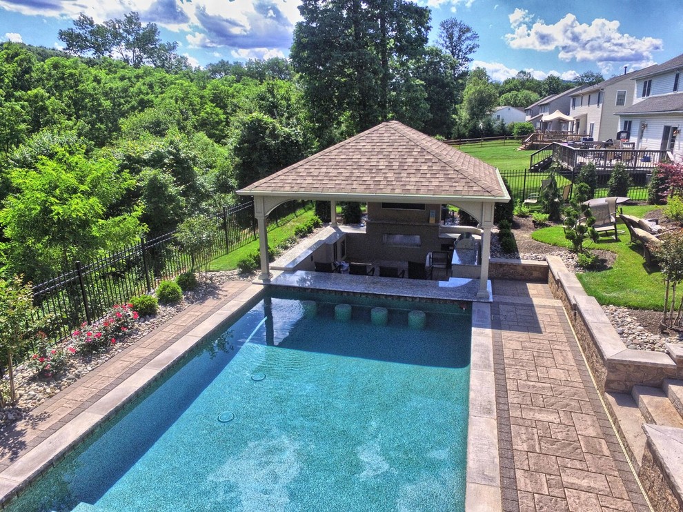 Modelo de casa de la piscina y piscina alargada tradicional renovada grande rectangular en patio trasero con adoquines de hormigón