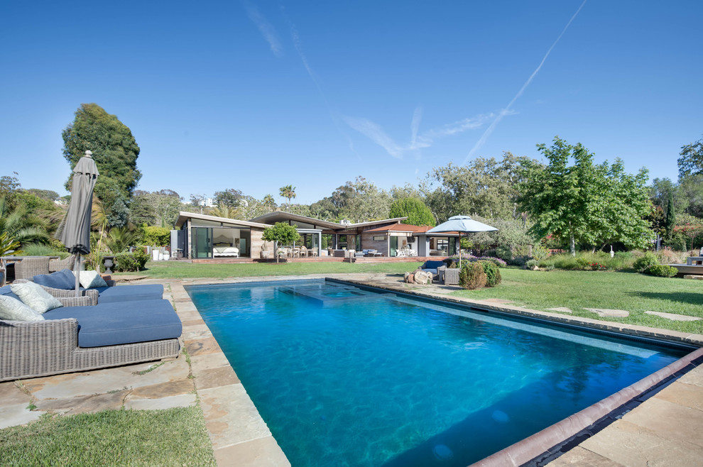 Ejemplo de piscina alargada retro grande rectangular en patio trasero con adoquines de piedra natural