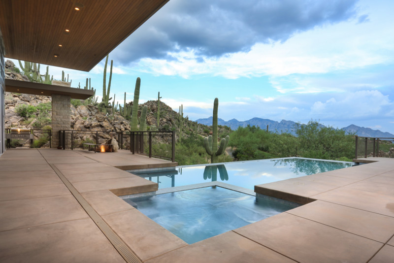 Inspiration for a large modern back custom shaped infinity swimming pool in Phoenix with concrete slabs.