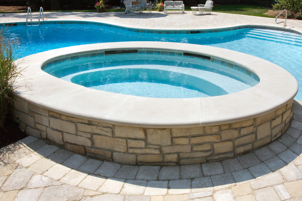 Идея дизайна: большой спортивный бассейн произвольной формы на заднем дворе в стиле неоклассика (современная классика) с джакузи и покрытием из каменной брусчатки