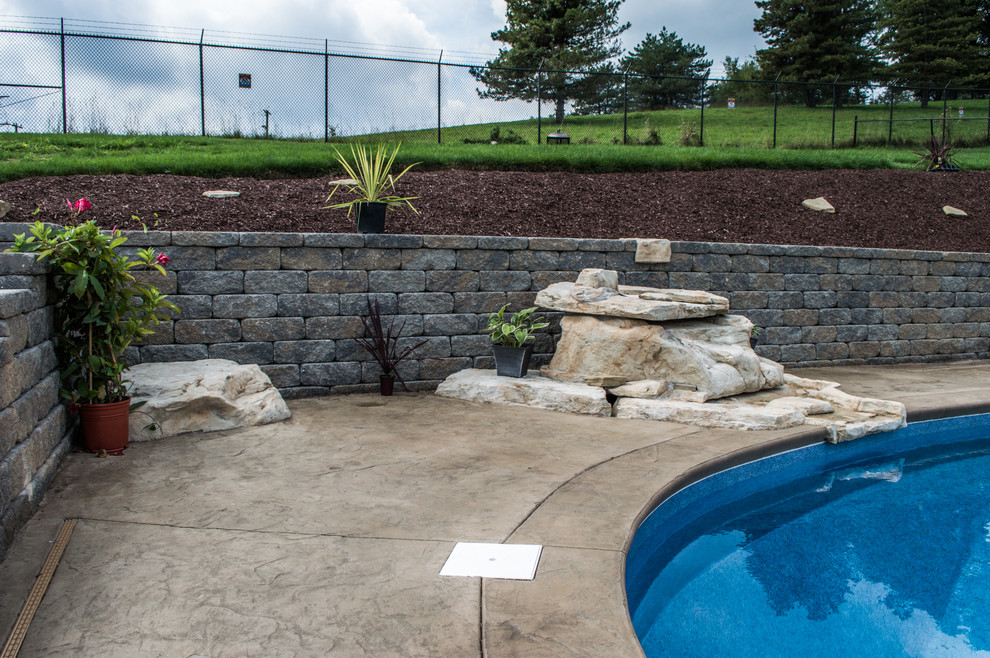 Modelo de piscina con fuente natural rural grande tipo riñón en patio trasero con suelo de hormigón estampado