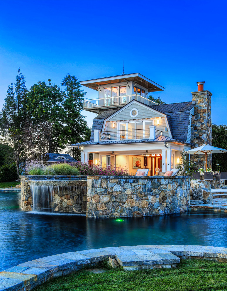 Foto di una grande piscina stile marinaro personalizzata dietro casa con fontane e pavimentazioni in pietra naturale