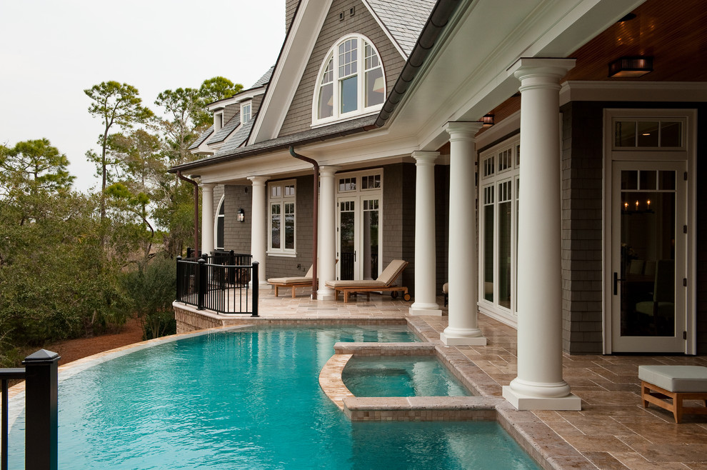 Ejemplo de piscina infinita tradicional grande a medida en patio trasero con adoquines de piedra natural