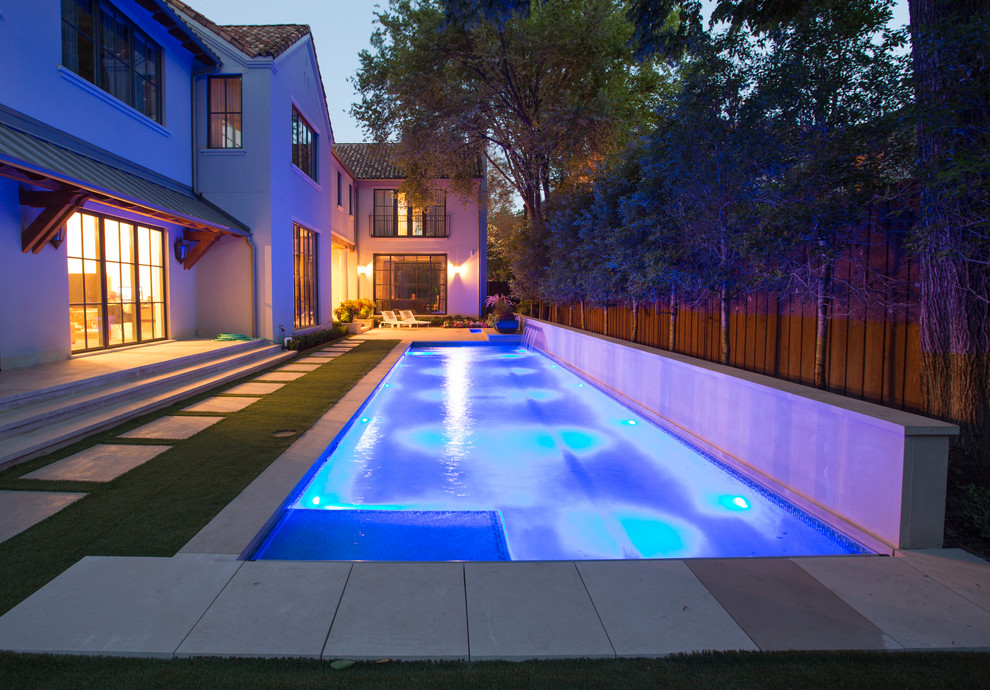 This is an example of a large traditional back rectangular lengths swimming pool in Dallas with a water feature and natural stone paving.