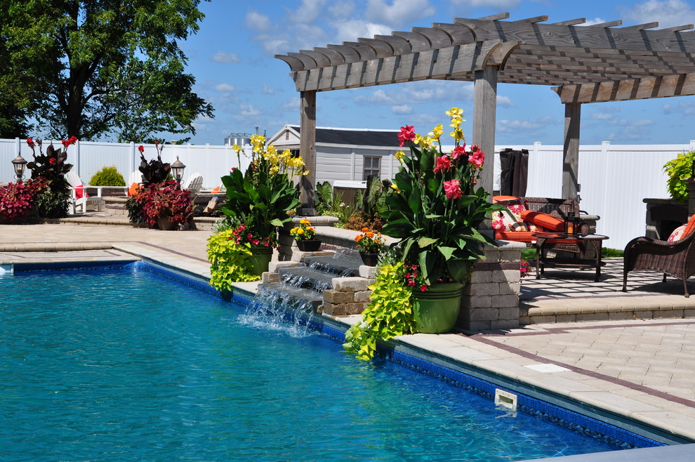 Diseño de piscina con fuente tropical extra grande rectangular en patio trasero con adoquines de ladrillo